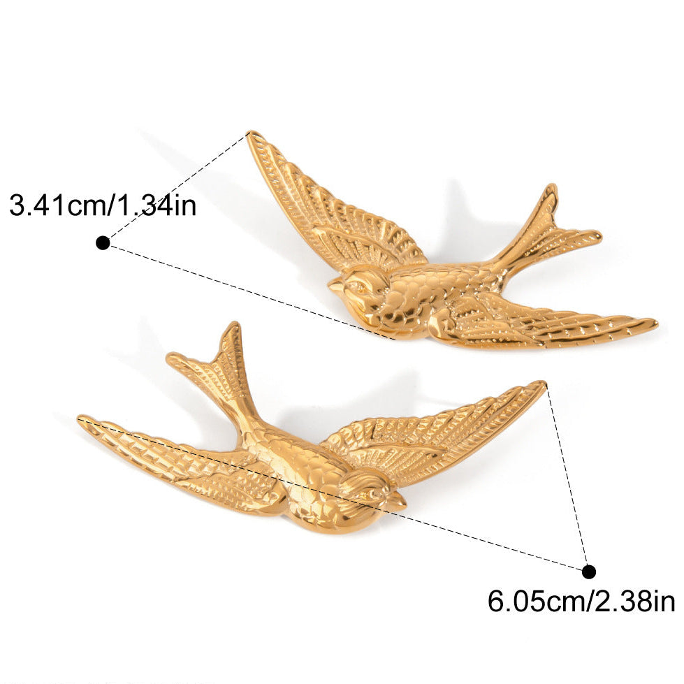 A close-up image of a person wearing gold-colored stainless steel earrings shaped like birds.